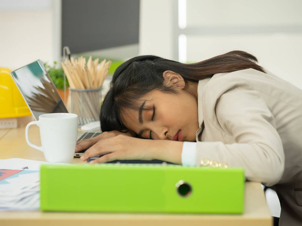 Biznesmenka i pracownik zdrzemnęli się pracując przy biurku. Pracujące kobiety są wyczerpane i śpią na stole. - Zdjęcie, obraz