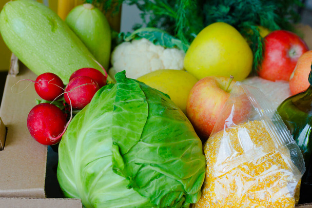 Volle Schachtel mit Obst und Gemüse Äpfel Kohl aus nächster Nähe. Essenslieferdienste während der Coronavirus-Pandemie und soziale Distanzierung. Online einkaufen. Essensspenden. - Foto, Bild