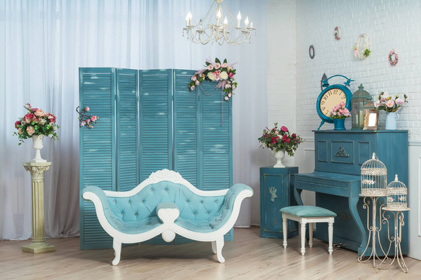 Sofá clásico azul claro en el fondo de una pantalla plegable en la sala de estar. Salón blanco de estilo clásico con piano azul. Decoración interior primavera verano
 - Foto, Imagen