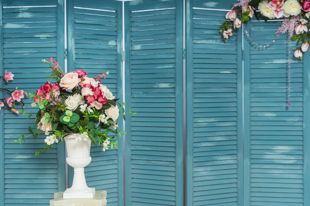 Bloemen in witte vaas op blauwe vouwscherm achtergrond. Blauw houten vouwscherm met glazen kralen bloemstuk decor. Houten louvre. Binnenlouver vouwscherm met bloemen - Foto, afbeelding