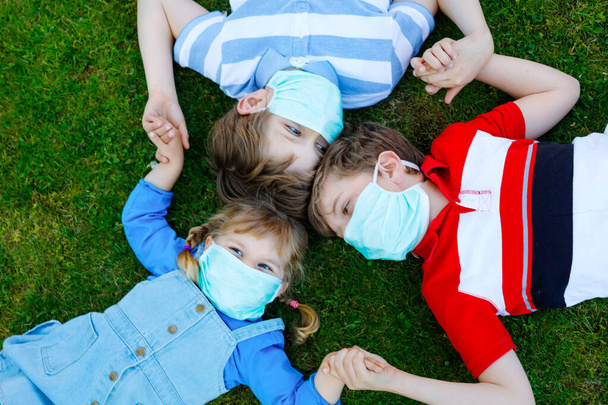 three kids, little toddler girl and two kid boys in medical mask as protection against pandemic coronavirus disease. Children, lovely siblings using protective equipment as fight against covid 19. - Φωτογραφία, εικόνα