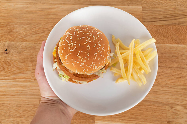 Tasty cheeseburger with vegetables and sauce in a sesame bun and french fries on wooden table - Foto, Imagem