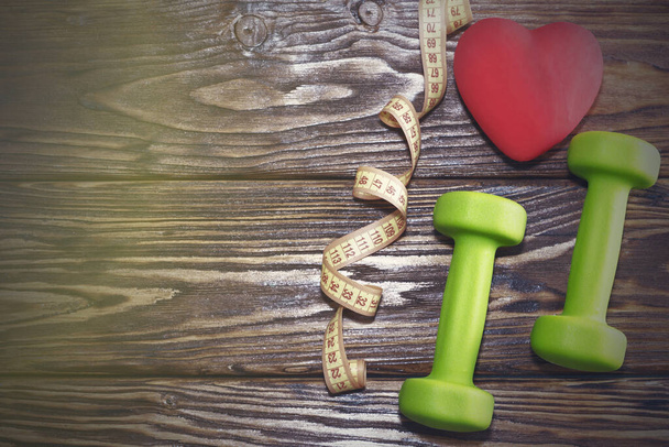Dumbbells and a red heart on a wooden background. The concept of a healthy lifestyle. - Photo, Image