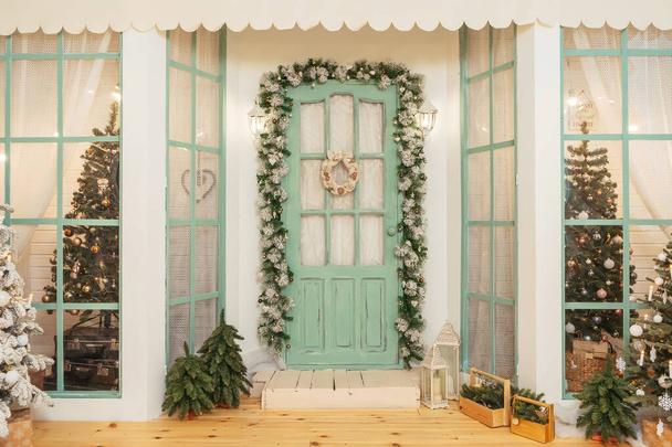 Portico con porta verde in addobbi natalizi e alberi di Natale. Ghirlande di abete intorno alla porta. Bella terrazza invernale della casa con ghirlande di lampadine retrò
 - Foto, immagini