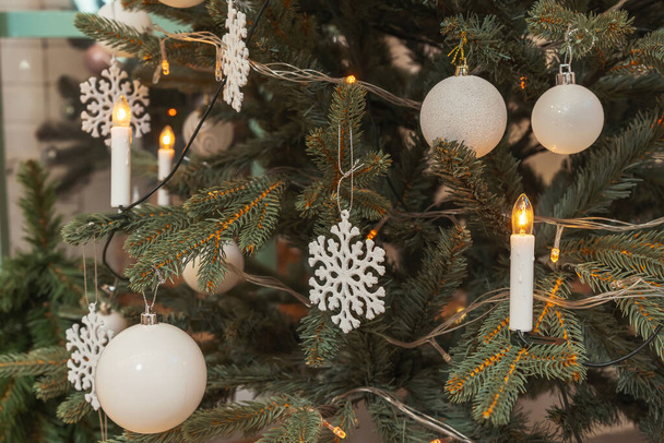 Girlanden in Form von Kerzen am Weihnachtsbaum. Weiße Dekorationskugeln Schneeflocken auf dem Weihnachtsbaum aus nächster Nähe. Gefälschter künstlicher Weihnachtsbaum - Foto, Bild