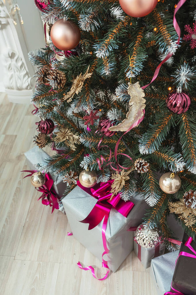 Κουτιά δώρου κάτω από το χριστουγεννιάτικο δέντρο με μπάλες κορδέλες γιρλάντες σε ροζ χρυσό καφέ στυλ διακόσμηση από κοντά. Όμορφη Χριστουγεννιάτικη διακόσμηση. Χριστουγεννιάτικα δέντρα με κώνους σε χρυσαφί ασημί χρυσόσκονη. - Φωτογραφία, εικόνα