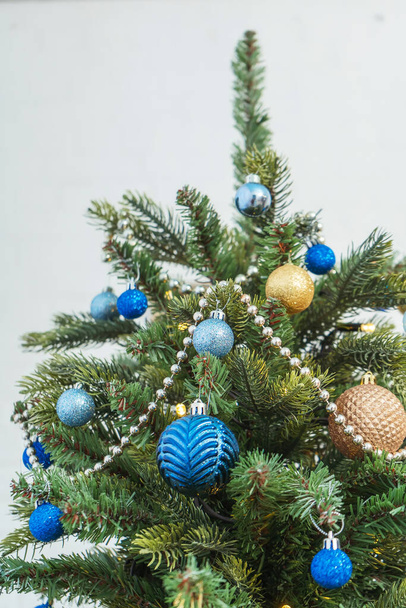 Gouden en blauwe ballonnen bovenop een kerstboom close-up. Kerst decoraties op de top van de kerstboom ballen slingers en kralen. Blauwe en gouden versiering van de nieuwjaarskaart - Foto, afbeelding