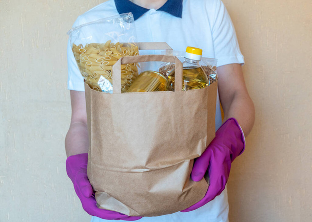 Волонтер в захисних рукавичках покласти їжу в коробку пожертвувань. Служба карантину пандемії коронавірусу
. - Фото, зображення