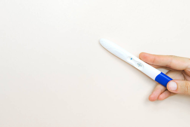 Woman hand holding a positive pregnancy test on pink background. - Foto, Bild