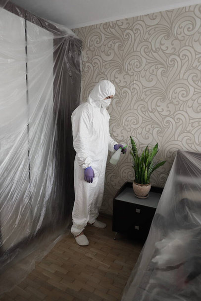 человек в защитном костюме, маске и перчатках поливает и распыляет цветок
 - Фото, изображение