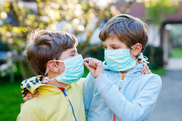 Dva chlapci v lékařské masce jako ochrana proti pandemické koronavirové chorobě. Děti, milí sourozenci a nejlepší přátelé používající ochranné prostředky jako boj proti covidu 19. - Fotografie, Obrázek