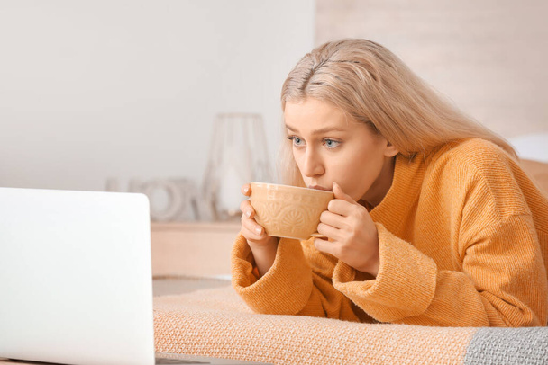 Beautiful young woman with laptop drinking tea at home - Фото, зображення