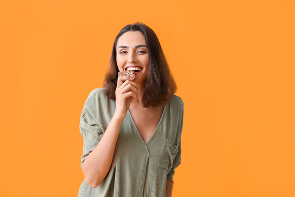 Beautiful young woman eating tasty chocolate on color background - Foto, Imagen
