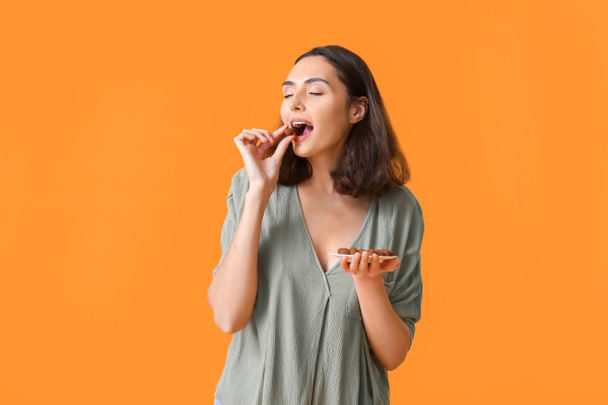 Όμορφη νεαρή γυναίκα τρώει νόστιμες καραμέλες σοκολάτας στο φόντο χρώμα - Φωτογραφία, εικόνα