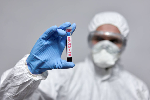 Doctor in overall protection suit with a test tube for coronavirus - Fotó, kép