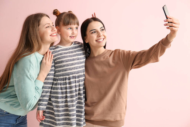 gelukkig lesbisch paar met weinig geadopteerd meisje nemen selfie op kleur achtergrond - Foto, afbeelding