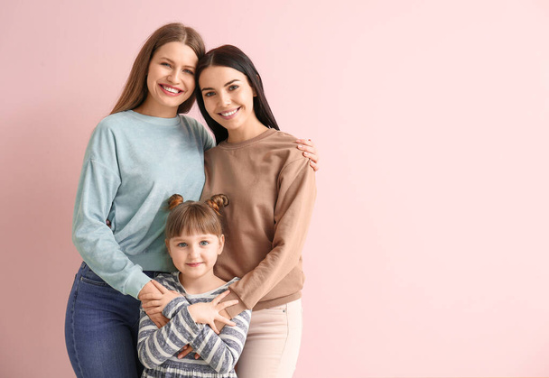 Happy lesbian couple with little adopted girl on color background - Photo, Image