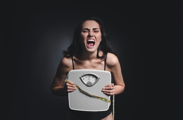 Sick woman with scales and measuring tape on dark background. Concept of anorexia - Photo, Image