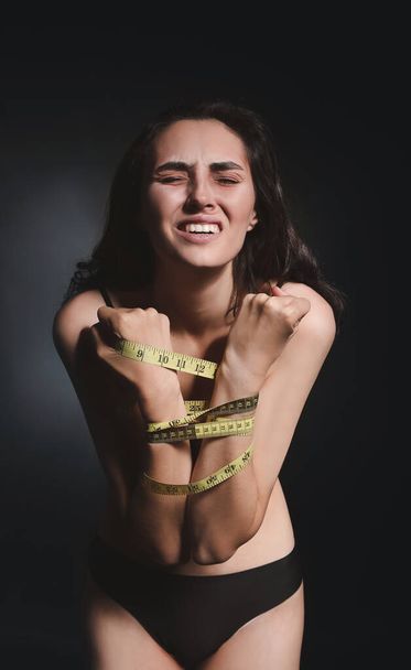 Mujer enferma con cinta métrica sobre fondo oscuro. Concepto de anorexia
 - Foto, imagen