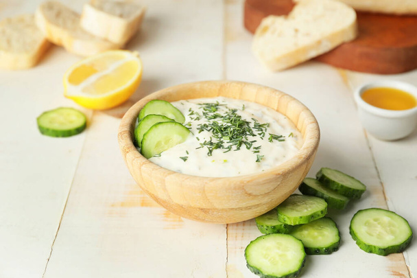 Heerlijke yoghurtsaus met komkommer in kom op witte tafel - Foto, afbeelding
