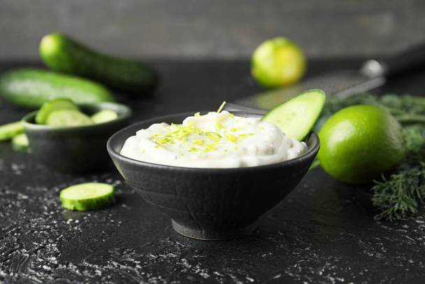 Delicious yogurt sauce with cucumber in bowl on dark background - Photo, image