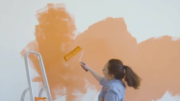 Singleton lifestyle and renovation concept. Young smiling woman with painting roller paints the wall in the apartment and dances - Footage, Video