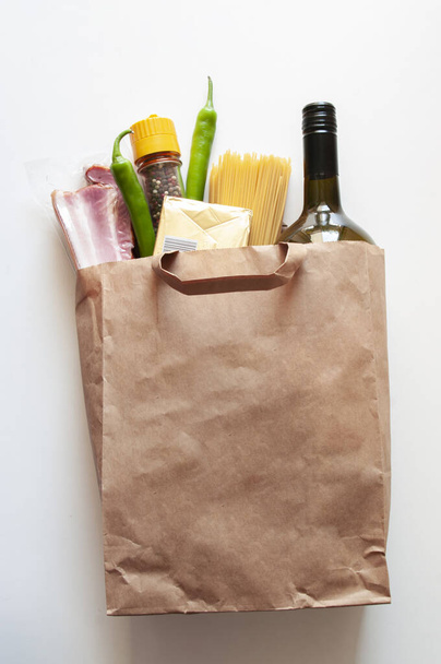 Paper bag with Food supplies, crisis food stock for quarantine isolation period,. salad, pasta, butter,wine,chilli, bacon. Food delivery, donation coronavirus. - Photo, Image