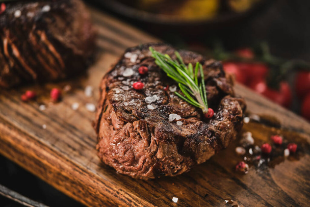 Grilled fillet steaks on wooden cutting board. Succulent thick juicy portions of grilled fillet steak served with tomatoes and roast potatoes on an old wooden board - 写真・画像