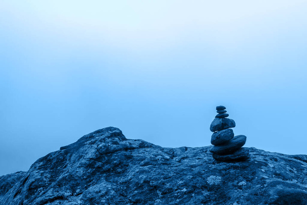 Minimalisme. Un petit cairn se dresse sur un grand rocher avec un brouillard dense en arrière-plan. Teinte bleue 2020. Horizontal
. - Photo, image
