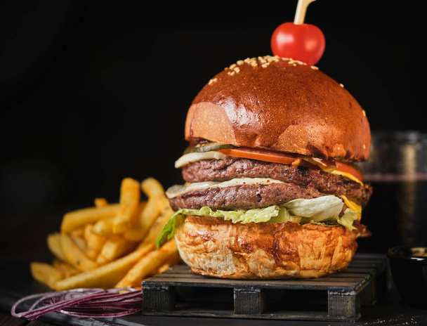 Double beef cheeseburger met Amerikaanse frietjes op een donkere achtergrond - Foto, afbeelding