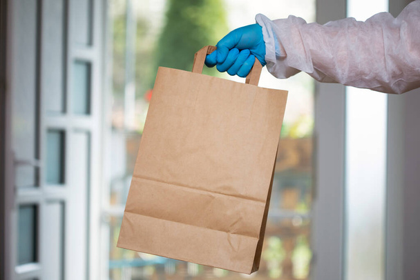 Man holding paper bag wearing blue glove as protection for COVID-19. Coronavirus pandemic precautions. - Photo, image