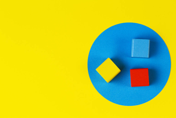 Blocos coloridos de madeira no fundo azul amarelo geométrico. Natural educacional zero resíduos de madeira brinquedos. Vista superior
 - Foto, Imagem