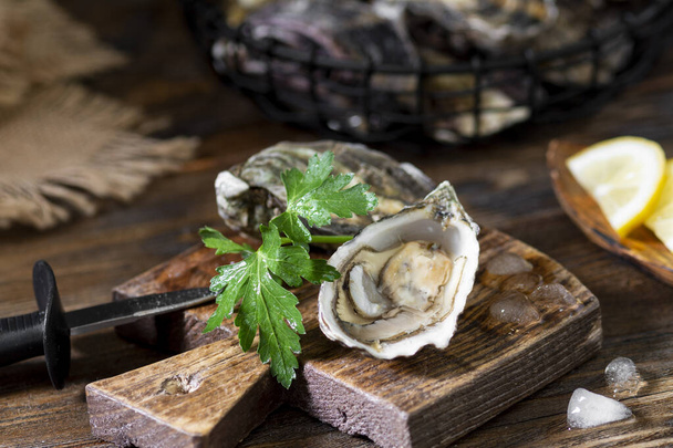 Two oysters on a wooden Board against the background of a basket of oysters - Fotografie, Obrázek