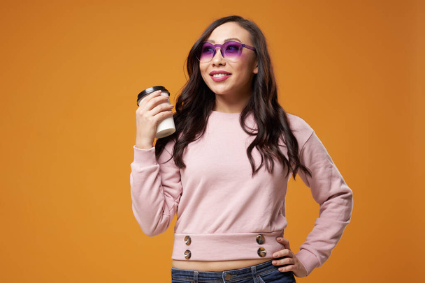 Cheerful woman in purple glasses with glass in her hands on orange background - Foto, Imagen