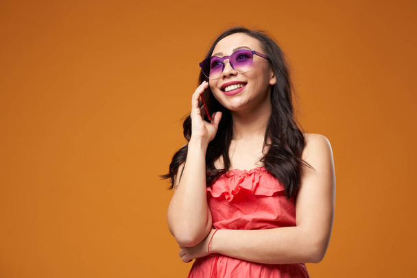 Happy woman in purple glasses talking on phone on empty orange background - Foto, imagen