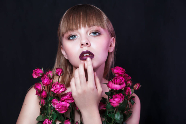 Fashion young woman with evening make-up posing in purple roses on black background - Fotó, kép