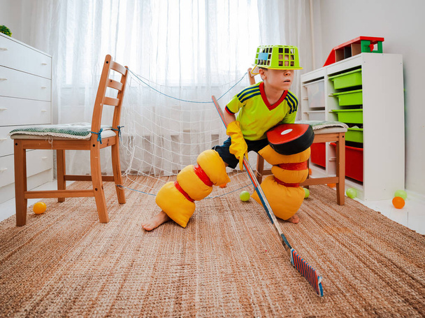 chłopiec gra w hokeja w domu zrobiwszy formę własnymi rękami z improwizowanych narzędzi bramy wykonane z krzeseł. Strona główna Improwizacja Dzieci zaradność gry dom dzieci sport dom kwarantanna - Zdjęcie, obraz
