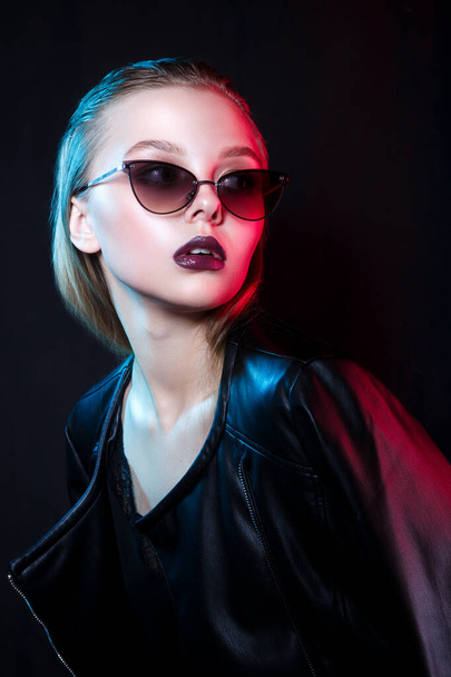 Fashion young model in sunglasses and stylish clothing on color neon lights in studio - Foto, Bild