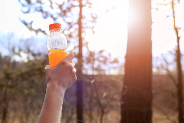Frauenhand mit Flasche Orangen-Smoothie an sonnigem Tag im Wald - Foto, Bild