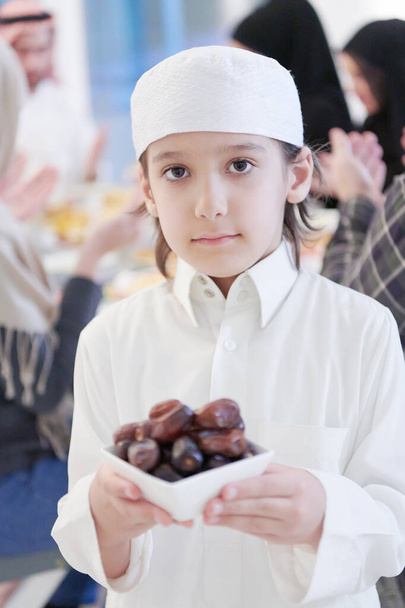 Eid Mubarak Muslim family having Iftar dinner little boy holding a plate full of sweet dates to break feast. Eating traditional food during Ramadan feasting month at home. The Islamic Halal Eating and Drinking at modern western Islam - Fotografie, Obrázek