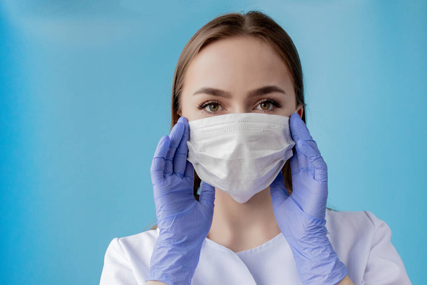 Doctor nurse smiling behind surgeon mask. Closeup portrait of young caucasian woman model on blue background. Woman wearing mass to protect covid-19. - Foto, imagen