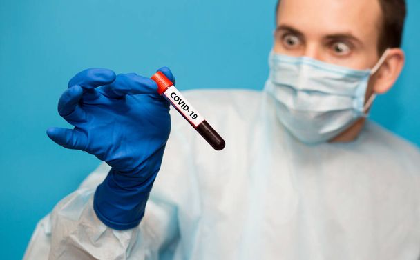 Medico in maschera protettiva e guanti isolati su sfondo blu detiene provetta contenente campione di sangue che ha testato per coronavirus. Test di laboratorio del sangue dei pazienti per la presenza di coronavirus COVID-19
. - Foto, immagini