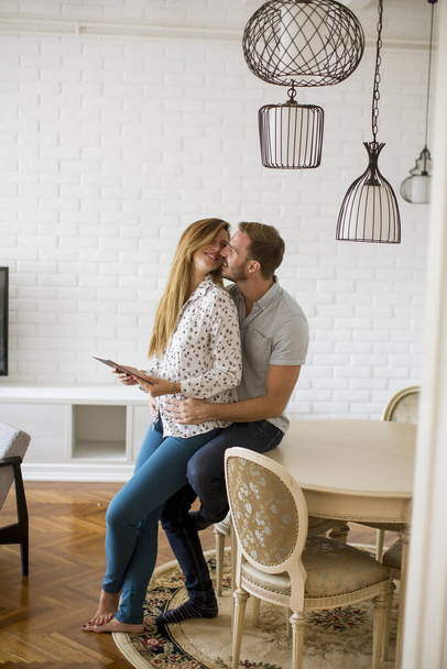 Ευτυχισμένο νεαρό ζευγάρι κοιτάζοντας ψηφιακή ταμπλέτα στο σαλόνι - Φωτογραφία, εικόνα