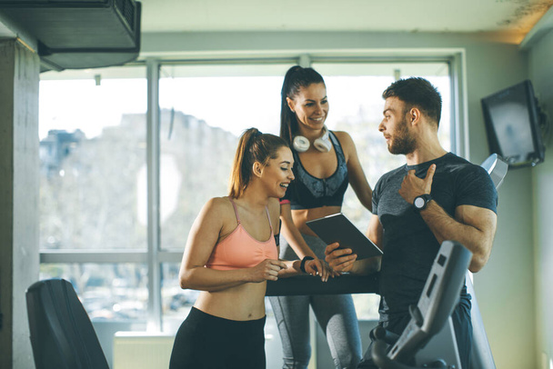 Personal trainer looking at digital tablet and explaining progress to young women at the gym - Fotoğraf, Görsel