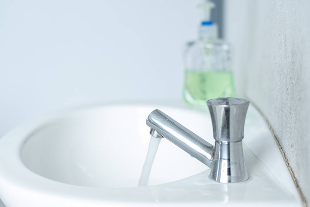 Elleri temizlemek için el dezenfektanıyla beyaz banyodaki suyu açan musluk.. - Fotoğraf, Görsel