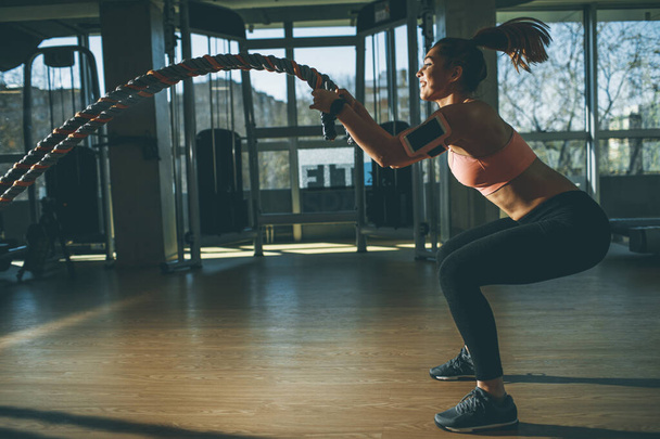 Pretty young woman with battle ropes exercise in the fitness gym - Photo, image