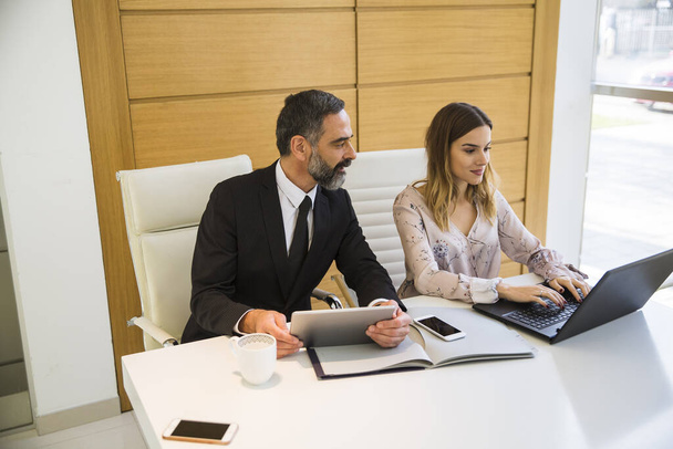 bel homme mature avec tablette numérique et jeune femme partenaires d'affaires avec ordinateur portable travaillant dans le bureau
 - Photo, image