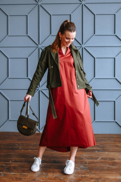 A model girl in a red dress, a green jacket and a purse. Demonstration of clothing for the showroom - Фото, зображення