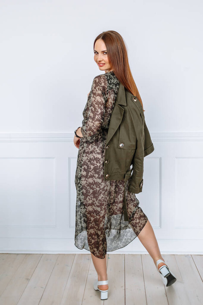 A model girl in a light dress and a green jacket. Demonstration of clothing for the showroom - Фото, изображение