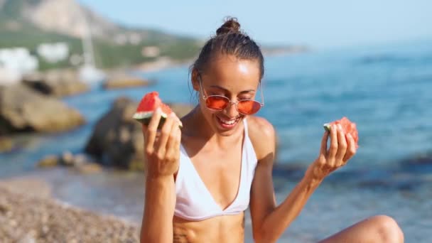 rozesmátá opálená dívka na pláži drží kousky melounu v obou rukou - Záběry, video